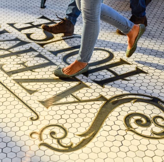people walking on tile floor with sazerac house logo emblem
